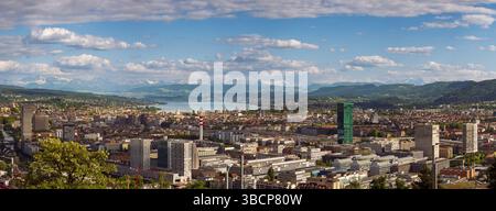 16-05-2025 Zurich, Suisse. Vue panoramique d'en haut comme vu d'un point de vue au sommet d'une colline. Ciel nuageux, Alpes enneigées et lac de Zurich dans le backgrou Banque D'Images