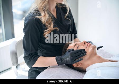 Cosmétologue faisant massage facial pour homme au salon de beauté Banque D'Images
