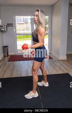 Femme brésilienne de 46 ans faisant des boucles biceps avec haltères vertical. Banque D'Images