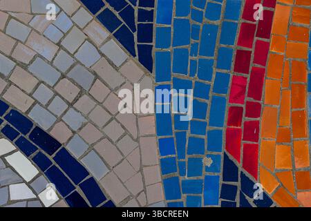 Gros plan d'un mur en mosaïque éclatante avec des rangées courbes de carreaux bleus, rouges, oranges et beiges disposés dans un design géométrique abstrait. Banque D'Images
