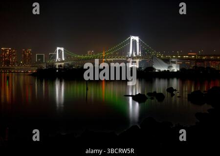 Pont arc-en-ciel illuminé enjambant la baie de Tokyo la nuit, avec son reflet scintillant dans les eaux calmes Banque D'Images