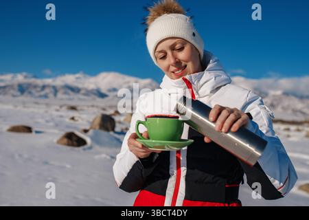 Jeune femme touriste dans les montagnes versant le thé du thermos dans la tasse en hiver Banque D'Images