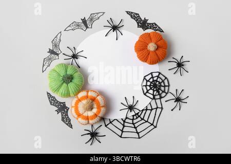 Composition d'Halloween de citrouilles tricotées orange et vertes, de toiles d'araignée noires et d'araignées et de chauves-souris avec un endroit blanc rond pour le texte. Jouets tricotés faits à la main pour enfants et décoration de maison de vacances. Banque D'Images