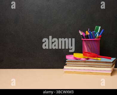 Une pile de livres colorés, un verre rose avec des stylos et des crayons, et deux loupes symbolisant l'apprentissage, la connaissance ou l'éducation sont placés dessus Banque D'Images