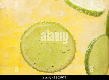 Eau gazeuse rafraîchissante avec des tranches de citron vert et de glace dans un verre sur fond orange, gros plan Banque D'Images