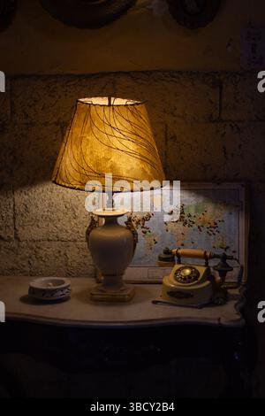 Lampe de chevet diffusant une lueur chaude dans une pièce faiblement éclairée la nuit, avec un téléphone vintage et une carte du monde en arrière-plan Banque D'Images