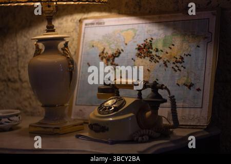 Lampe de chevet diffusant une lueur chaude dans une pièce faiblement éclairée la nuit, avec un téléphone vintage et une carte du monde en arrière-plan Banque D'Images