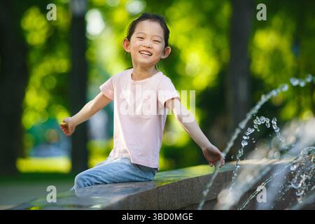 Happy Child Asian Girl jouant par Fountain dans Green Park le jour ensoleillé de l'été Banque D'Images