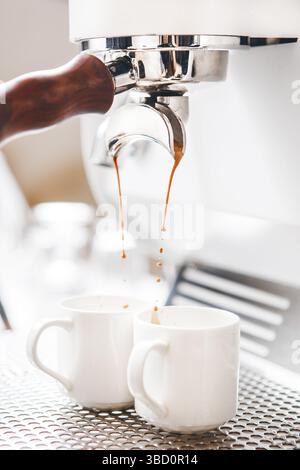 La machine à café blanche professionnelle prépare un double espresso dans un cadre lumineux avec deux tasses sous le bec verseur Banque D'Images