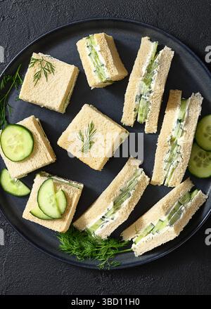 sandwichs au concombre superposés avec du fromage à la crème étalé sur une plaque noire sur une table en béton, vue horizontale d'en haut, pose à plat, gros plan Banque D'Images