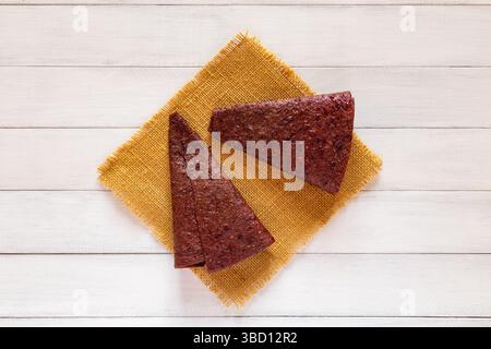 Deux morceaux de pastille de fruits triangulaires rouges affichés sur tissu jaune sur fond de bois blanc à partir de l'angle supérieur Banque D'Images