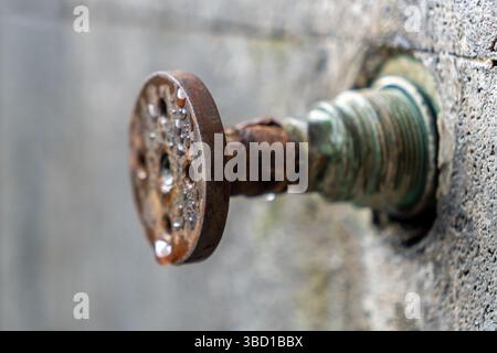 Robinet rouillé avec de l'eau qui s'égoutte de lui. Les gouttelettes d'eau sont petites et dispersées, donnant l'impression d'une pluie légère. Le robinet est vieux et percutant Banque D'Images