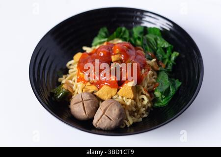 Indonésien Mie Ayam avec Bakso servi sur bol noir, une cuisine traditionnelle indonésienne. Nouilles asiatiques avec boulettes de viande, poulet et légumes frais Banque D'Images