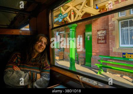 Jeune femme est assise et regarde rêvement par une fenêtre dans un wagon d'un train à vapeur à la gare Horsted Keynes, Bluebell Railway. Line, Sussex, Angleterre. Banque D'Images