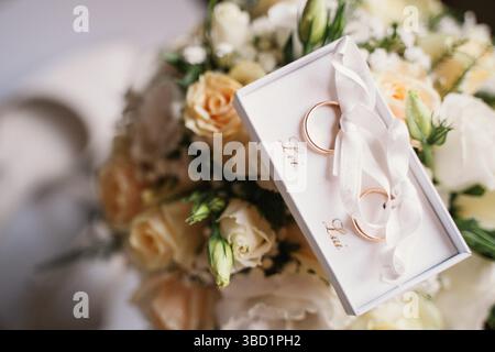 Gros plan de deux élégantes bagues de mariage dans une boîte blanche placée sur un bouquet floral vibrant. L'image capture l'essence de l'amour et de l'engagement, perfec Banque D'Images