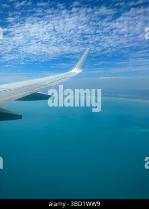 Vue aérienne depuis la fenêtre de l'avion montrant l'aile au-dessus des eaux turquoises de l'océan et un ciel bleu partiellement nuageux. Banque D'Images