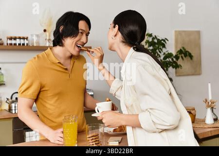 Un couple profite d'un moment léger tout en partageant une collation et des boissons à leur table de cuisine. Banque D'Images
