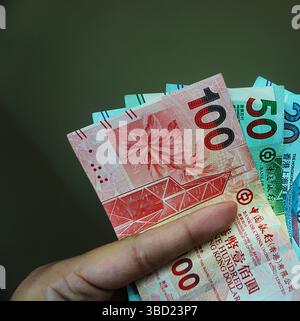 Dollars de Hong Kong en 100, 50 et 20 coupures tenues entre les doigts sur un fond clair. Banque D'Images
