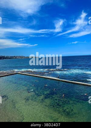 Piscine panoramique sur l'océan avec des nageurs profitant de l'eau cristalline sous un ciel bleu vif, surplombant la vaste côte de l'océan Pacifique. Banque D'Images