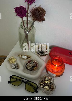 Table de chevet confortable avec affichage de bijoux, fleurs décoratives et une bougie incandescente créant une atmosphère chaleureuse et accueillante. Banque D'Images