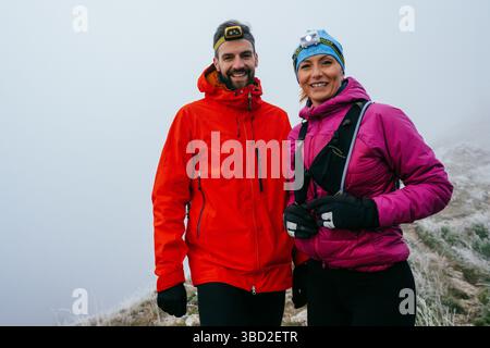 Randonneurs posant sur Foggy Mountain Top.Portrait de deux randonneurs posant ensemble sur un haut de montagne brumeux portant des équipements de plein air. Banque D'Images