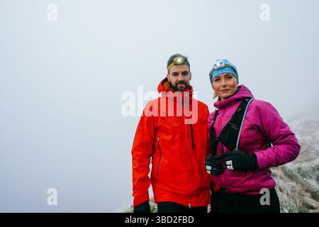 Randonneurs posant sur Foggy Mountain Top.Portrait de deux randonneurs posant ensemble sur un haut de montagne brumeux portant des équipements de plein air. Banque D'Images