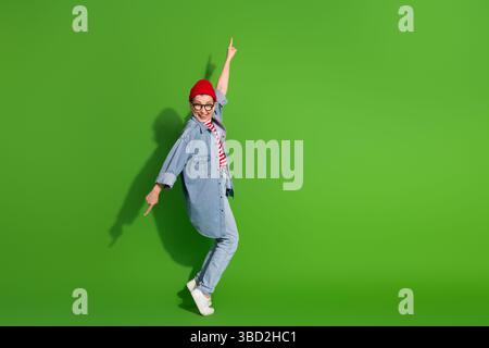 Femme âgée joyeuse en denim et bonnet faisant des gestes ludiques sur fond vert Banque D'Images
