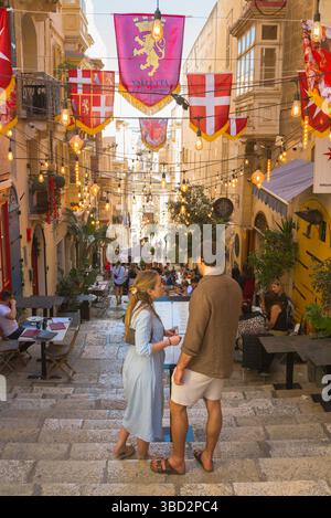 Malte Valette été, vue de deux jeunes touristes debout dans une rue populaire contenant des cafés et des restaurants dans le centre historique de la Valette Banque D'Images