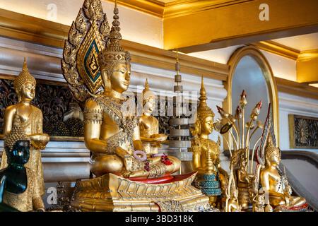 Une collection de statues de Bouddha dorées exposées dans un intérieur de temple thaïlandais orné. L'image capture les conceptions complexes et l'atmosphère spirituelle. Banque D'Images