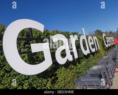 Panneau d'entrée blanc graphique Garden Centre, sous un soleil printanier lumineux avec des chariots à plantes au premier plan. Surrey Royaume-Uni Banque D'Images