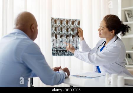 Femme médecin noire démontrant les rayons X à un patient masculin pendant la réunion à la clinique Banque D'Images