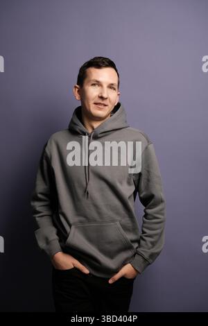 Un portrait décontracté mettant en vedette un homme vêtu d'un sweat à capuche gris sur un fond violet éclatant Banque D'Images