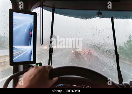 Vue intérieure du camion avec pare-brise couvert par une pluie intense, visibilité réduite sur la route et essuie-glaces luttant contre la tempête. Banque D'Images