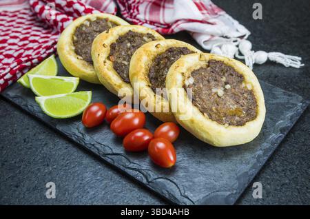 Délicieuse cuisine libanaise (arabe), véritables sfihas sur une plaque d'ardoise avec tomates et citrons à l'arrière-plan avec le keffiyeh libanais traditionnel (turba Banque D'Images