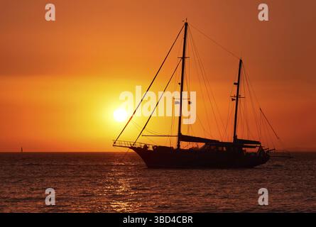 Vue rapprochée de la silhouette latérale du voilier avec des voiles vers le bas contre le soleil au coucher du soleil, l'éblouissement du soleil sur les eaux de mer. Paysage marin romantique. Voilier aller à la mer Banque D'Images