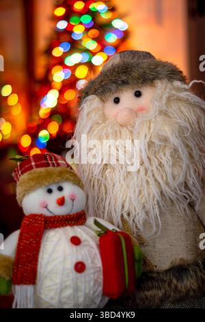 Frosty les figurines de bonhomme de neige et de Père Noël avec les lumières d'un arbre de Noël en arrière-plan Banque D'Images