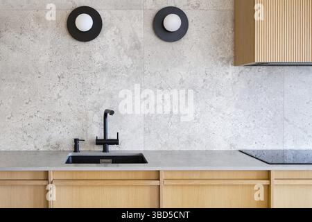 Intérieur de cuisine contemporain et minimaliste avec un évier noir élégant et un robinet serti contre un mur gris texturé, complété par deux circula modernes Banque D'Images