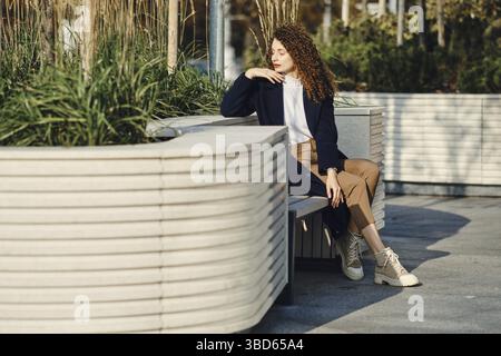 Jeune femme pensive assise sur un banc dans la ville Banque D'Images