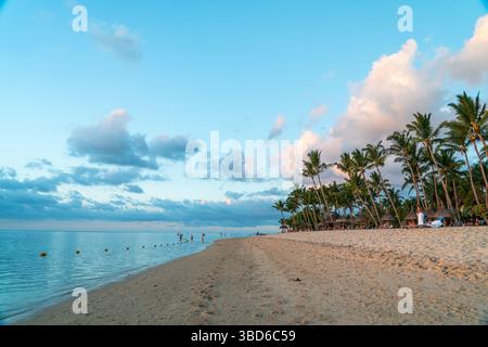Le Morne, Maurice - 12 mai 2024 : une plage côtière pittoresque avec des palmiers et des touristes profitant du coucher du soleil Banque D'Images