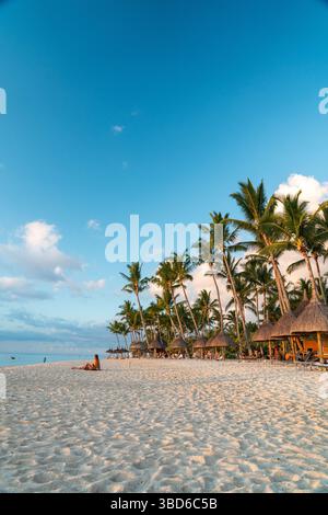 Le Morne, Maurice - 12 mai 2024 : une plage tropicale pittoresque avec des palmiers et un ciel bleu lumineux au coucher du soleil Banque D'Images