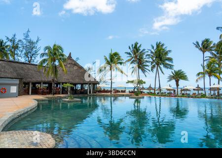 Le Morne, Maurice - 12 mai 2024 : une luxueuse piscine à débordement à côté d'une plage tropicale avec parasols et palmiers dans un complexe de l'île Maurice Banque D'Images