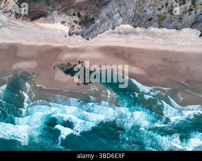 Vue aérienne par drone des vagues roulant vers une plage rocheuse encadrée par des falaises Banque D'Images