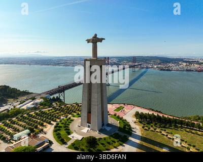 Almada, Portugal - 14 mai 2024 : monument du Christ Roi vu d'un angle élevé avec le Tage et le pont suspendu emblématique en vue Banque D'Images