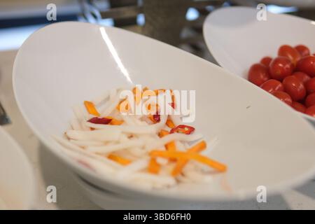 Des tranches de carottes fraîches pelées et de radis daikon, la moitié des radis daikon non pelés reposent sur une table blanche. Carotte, radis daikon, ingrédients populaires dans les salades de légumes et les collations Banque D'Images