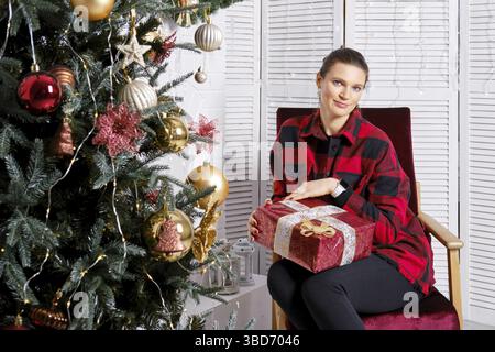 Femme souriante en chemise à carreaux et pantalon serré tient la boîte cadeau de noël à la main Banque D'Images
