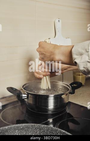 Femme méconnaissable mettant des nouilles de riz dans l'eau bouillante Banque D'Images