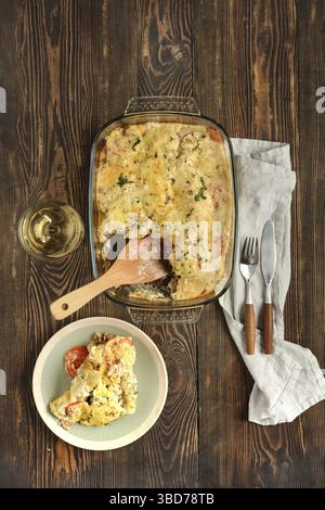 Une casserole cuite présentant des couches de pâtes cannelloni, des légumes et du fromage fondu accompagné d'un verre de vin et d'ustensiles soigneusement disposés Banque D'Images