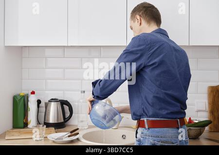 Vue arrière d'un homme d'âge moyen lave les plats après avoir cuisiné à la maison Banque D'Images