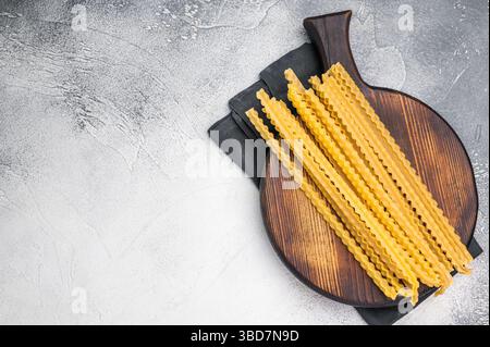 Délicates nouilles crues à base de mafaldine, parfaites pour les mélanger avec des ingrédients frais et des sauces salées. fond blanc. vue de dessus. Banque D'Images