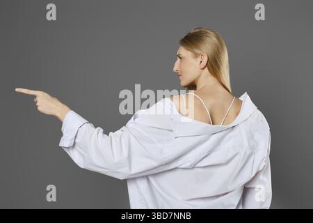 Vue de côté arrière d'une femme portant une chemise blanche pointant vers le côté avec l'index Banque D'Images